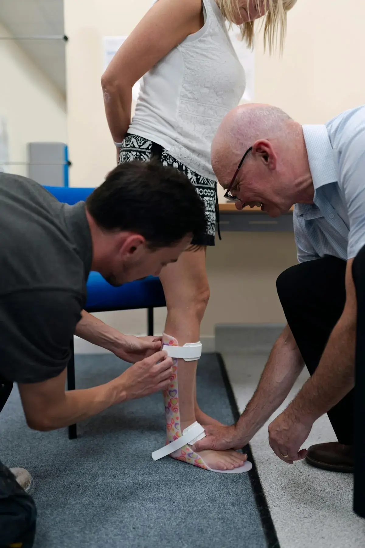 Two healthcare professionals fitting an ankle-foot orthosis brace on a patient's leg in a clinical setting