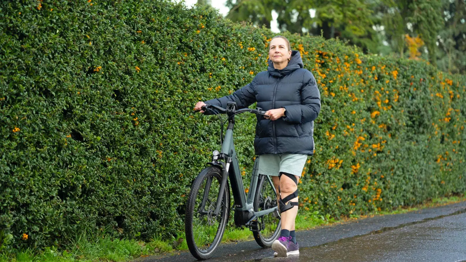 A woman wearing an Össur Unloader One X OA knee brace walks alongside a bicycle, remaining active outdoors