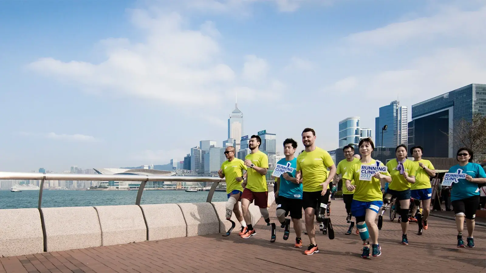 A group of amputee athletes wearing running blade prosthetics jog together along a waterfront at an Ottobock Running Clinic